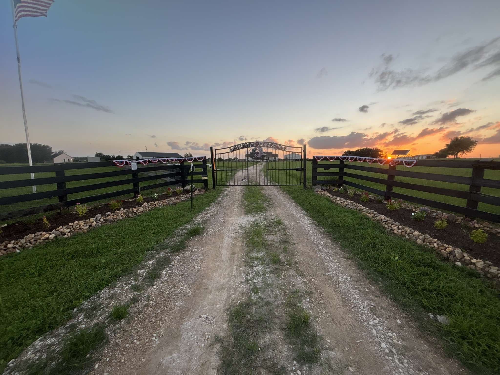 The front gate and drive at dusk, the sky glowing orange behind