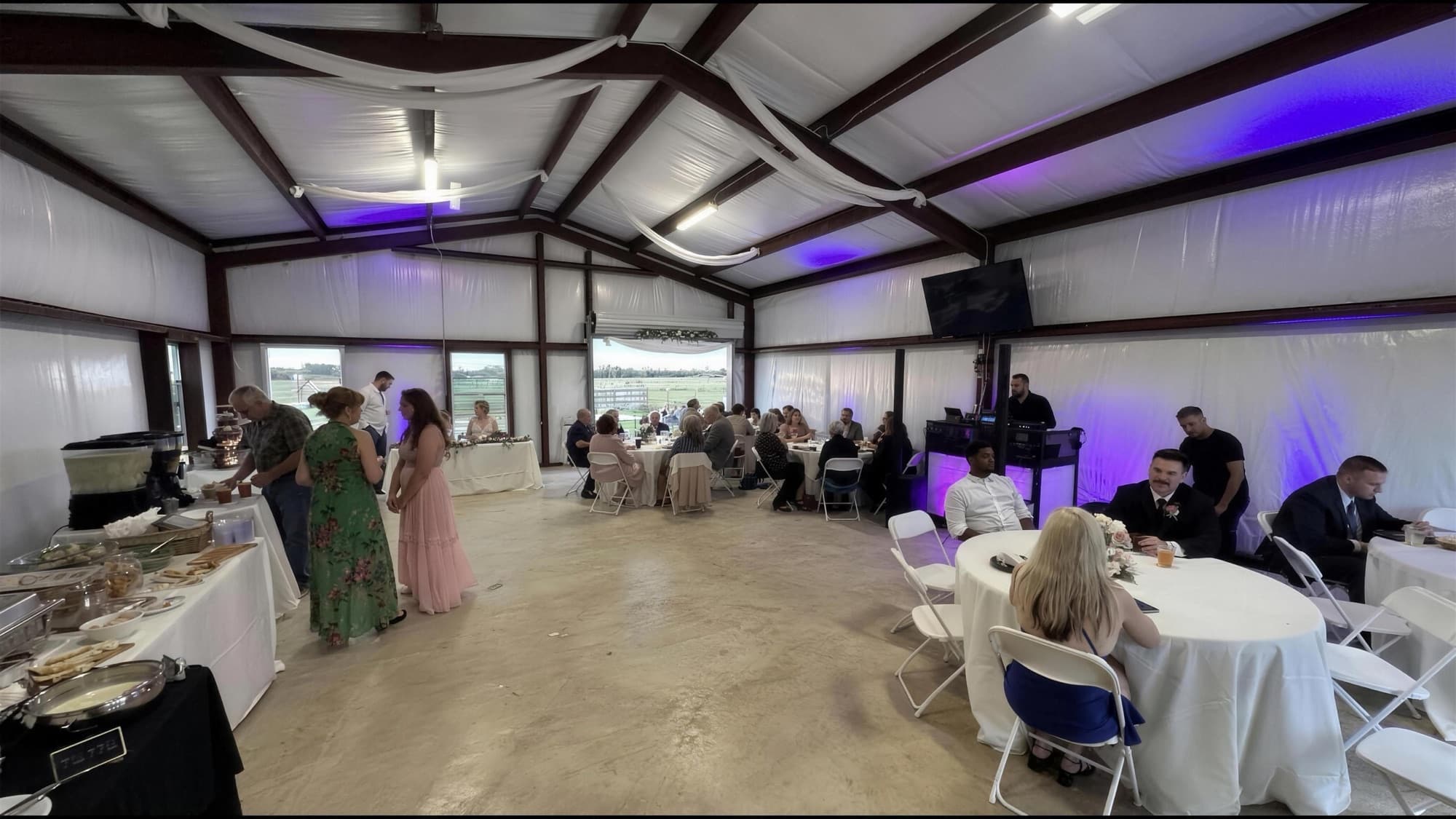 Long tables set for a reception dinner under a decorated barn