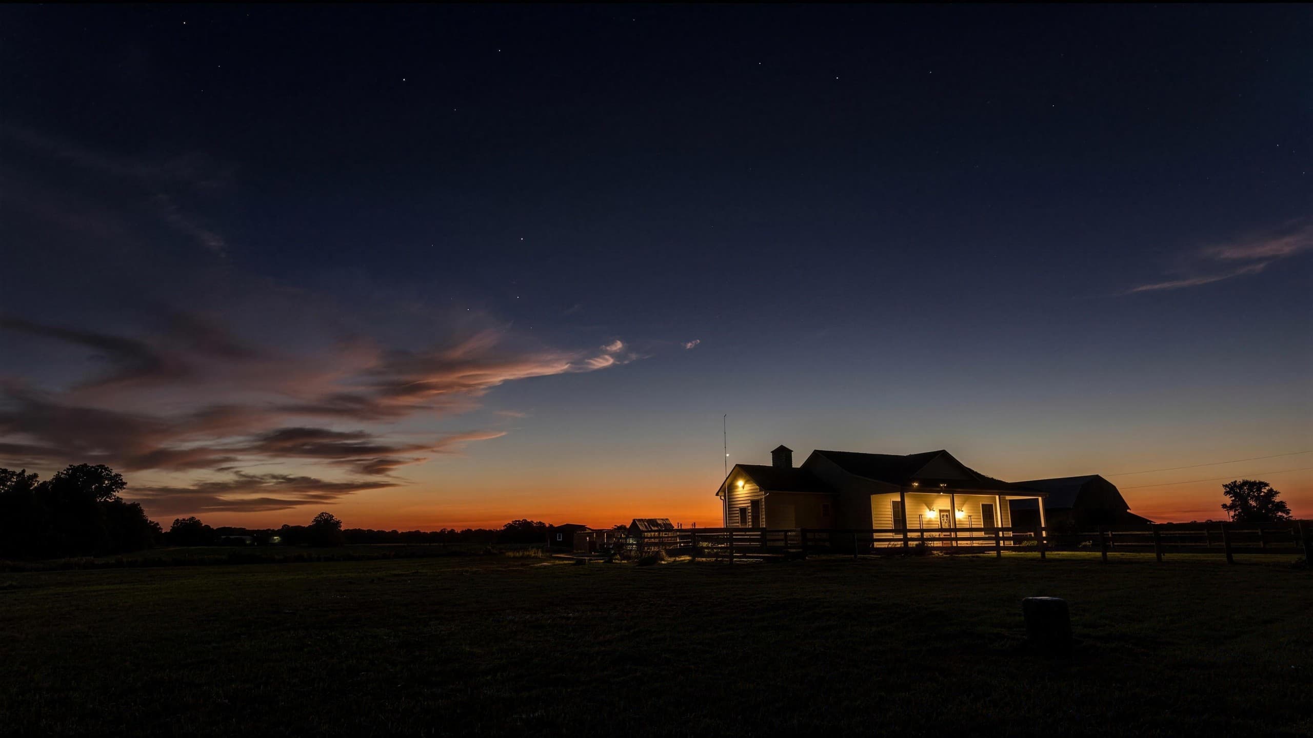 The farmhouse lit up at dusk under a deep orange and blue sky with the first stars showing