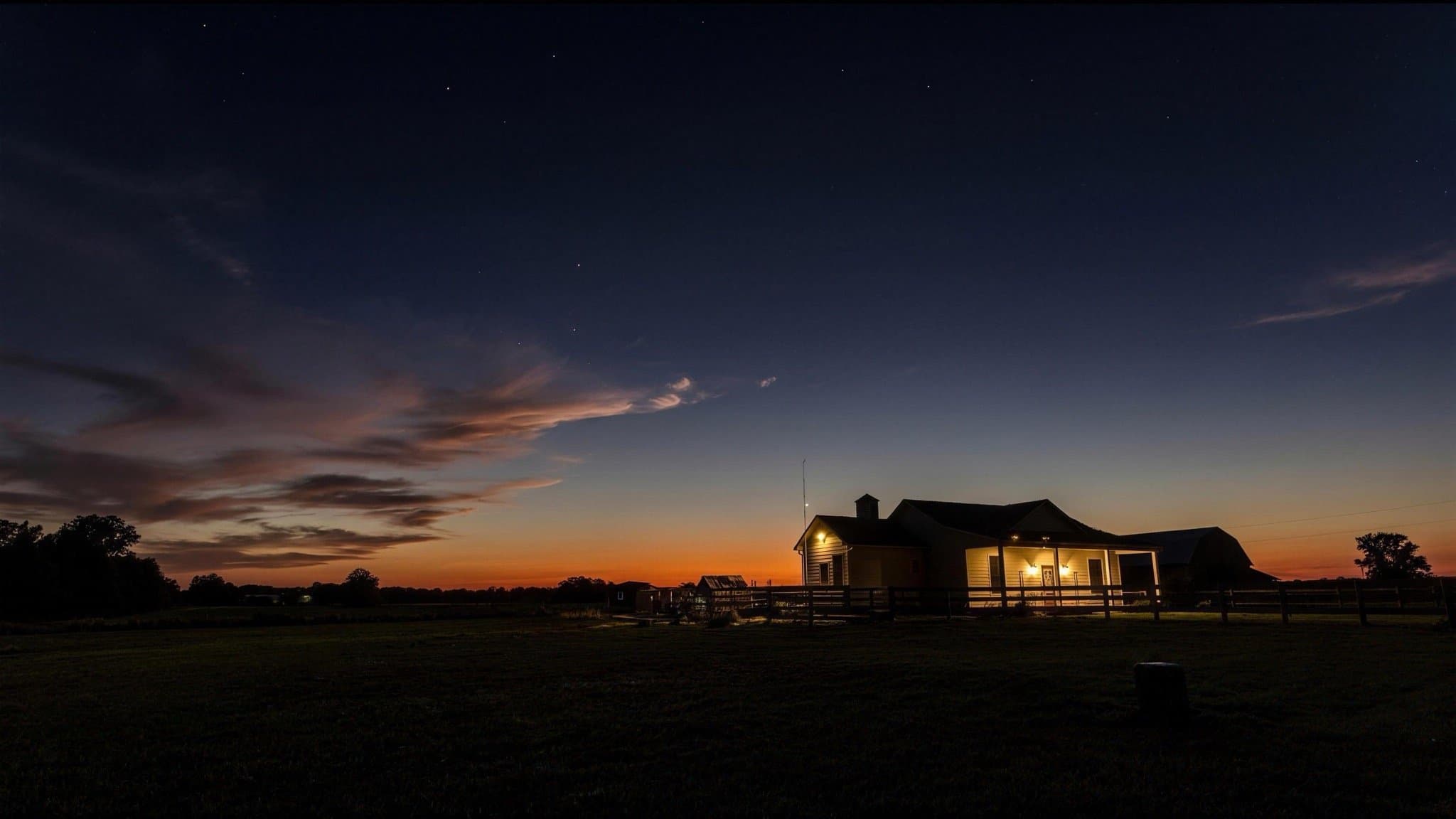 The farmhouse in silhouette against a warm sunset sky