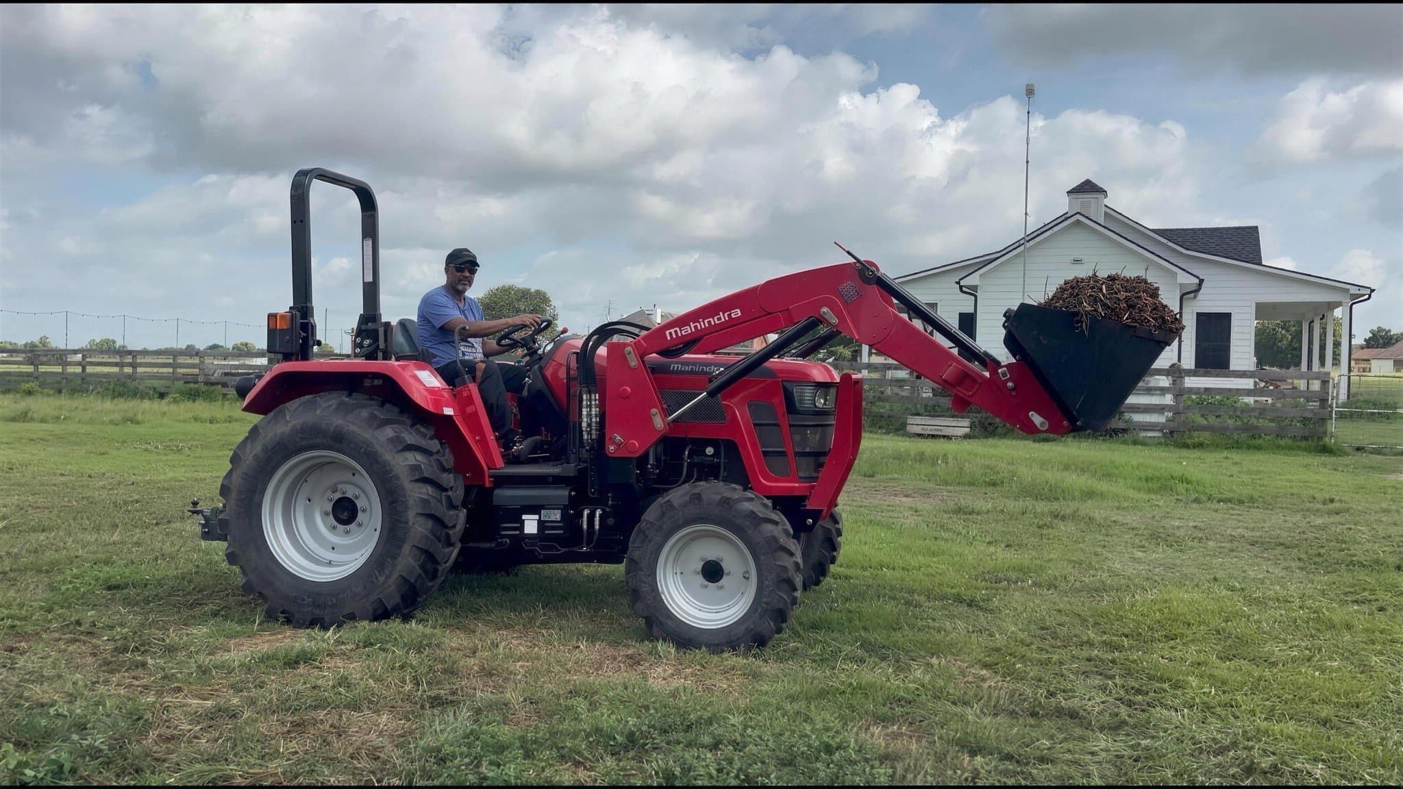 A man on a red tractor lifting a loader bucket of mulch, the white farmhouse behind.