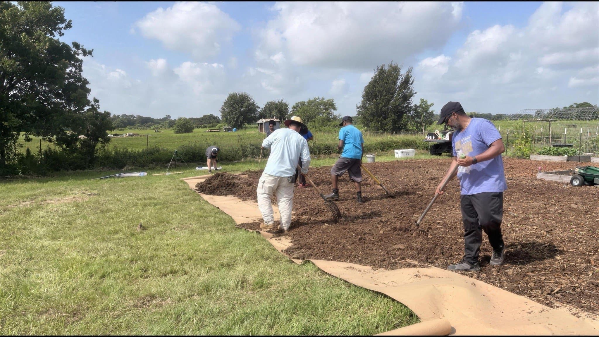 A group of volunteers raking and prepping a large garden bed together.