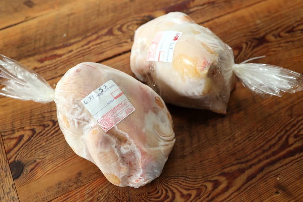 Two whole farm-raised chickens, processed and packaged for the freezer, on a wooden table.